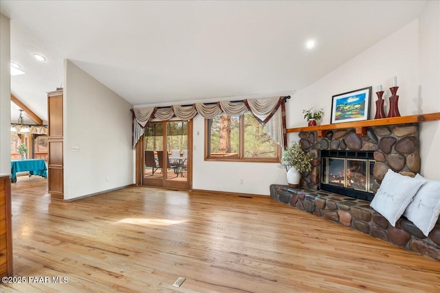 living room featuring a stone fireplace, light wood-style flooring, and vaulted ceiling