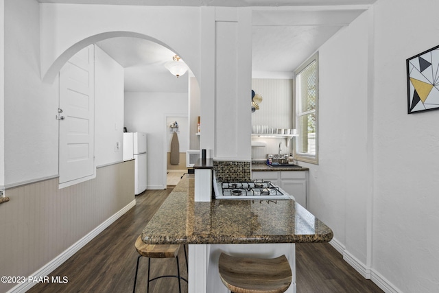 kitchen with dark wood-type flooring, dark stone counters, white appliances, a kitchen bar, and white cabinets