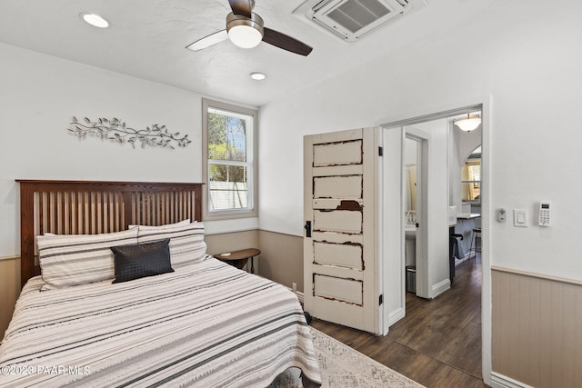 bedroom featuring visible vents, dark wood finished floors, arched walkways, wainscoting, and ceiling fan