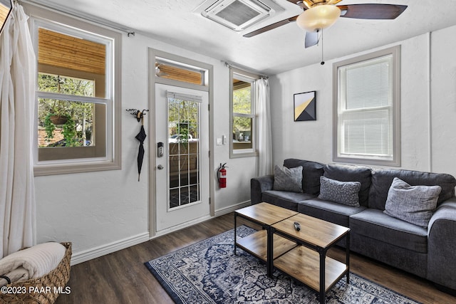 living room with a ceiling fan, visible vents, baseboards, dark wood-style flooring, and a textured wall