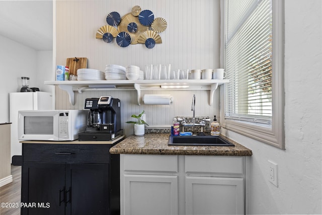 kitchen with open shelves, wood finished floors, white microwave, and a sink