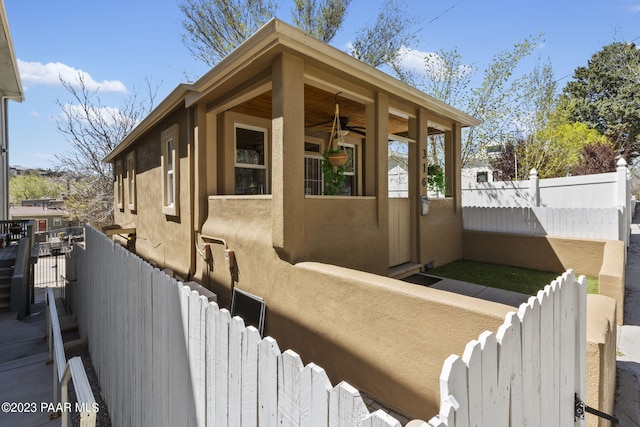 view of side of property featuring stucco siding, ceiling fan, and fence