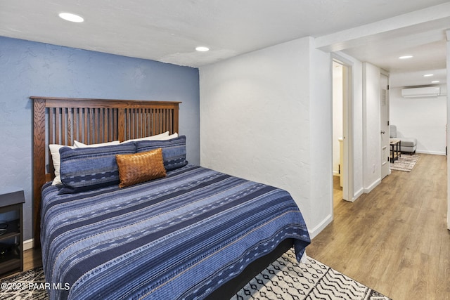 bedroom featuring a wall unit AC, recessed lighting, wood finished floors, and baseboards