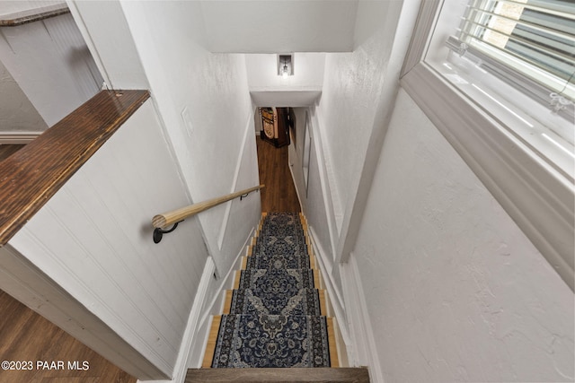 stairs with wood finished floors and a textured wall