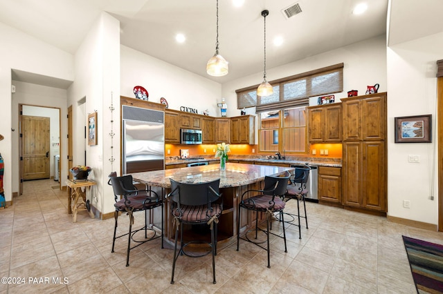 kitchen with light stone countertops, stainless steel appliances, high vaulted ceiling, a kitchen island, and hanging light fixtures