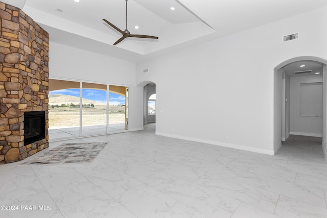 unfurnished living room featuring ceiling fan, a towering ceiling, a fireplace, and a tray ceiling