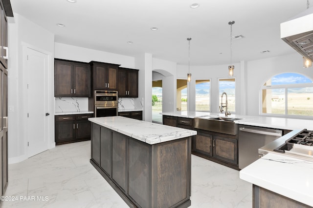 kitchen featuring appliances with stainless steel finishes, backsplash, dark brown cabinets, hanging light fixtures, and an island with sink