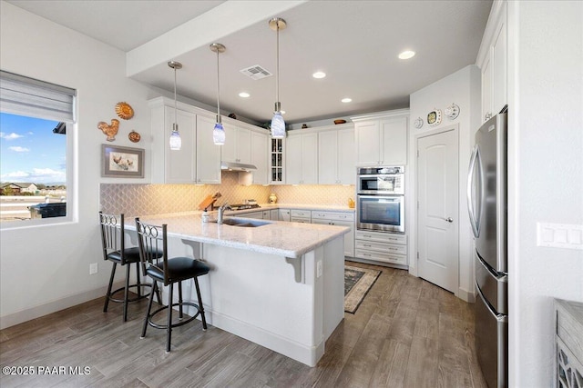 kitchen featuring visible vents, under cabinet range hood, backsplash, a peninsula, and appliances with stainless steel finishes