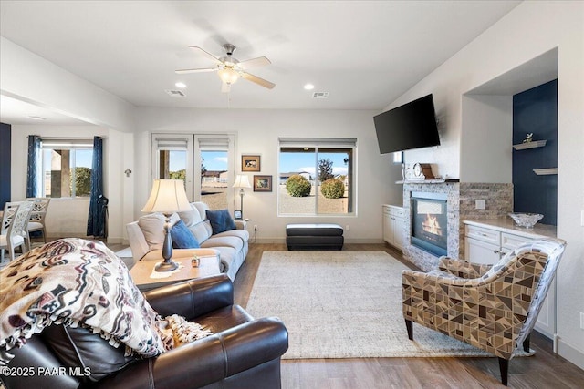living area featuring a glass covered fireplace, visible vents, ceiling fan, and wood finished floors