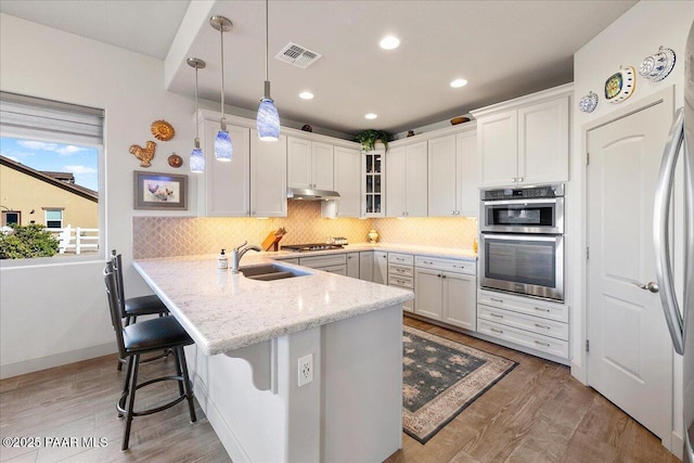 kitchen with visible vents, under cabinet range hood, appliances with stainless steel finishes, a kitchen breakfast bar, and a sink