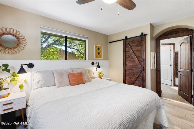714 Mingus Ave, Prescott, AZ 86301 - bedroom with a barn door, light wood-style flooring, wainscoting, arched walkways, and a ceiling fan