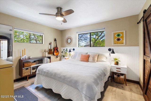 714 Mingus Ave, Prescott, AZ 86301 - bedroom featuring a barn door, light wood-style flooring, multiple windows, wainscoting, and ceiling fan