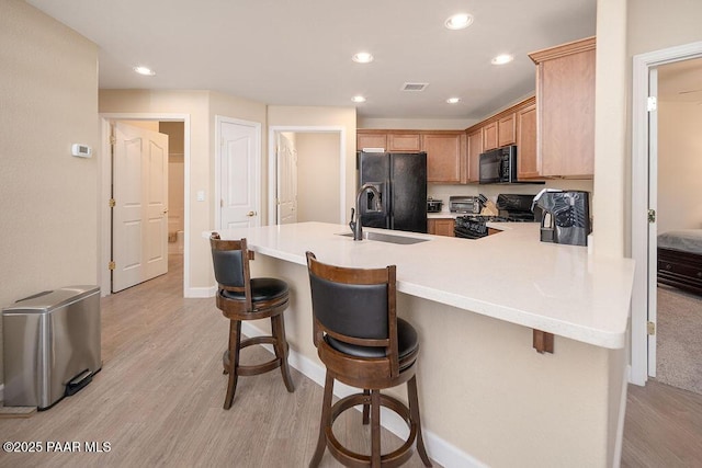 kitchen with a kitchen bar, kitchen peninsula, sink, and black appliances