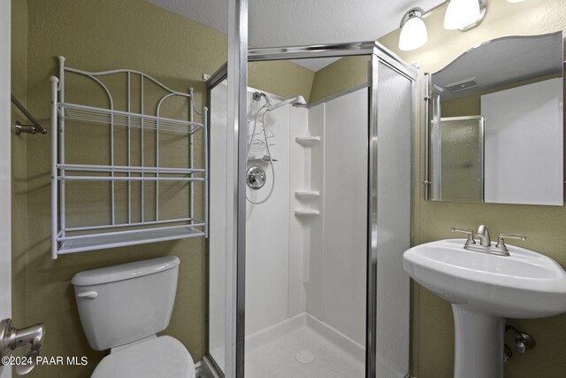 bathroom with toilet, a shower with door, and sink