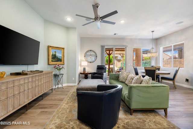 living room featuring baseboards, ceiling fan with notable chandelier, light wood finished floors, and plenty of natural light
