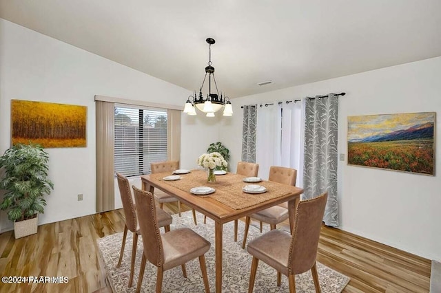 dining area with light hardwood / wood-style flooring, a chandelier, and vaulted ceiling