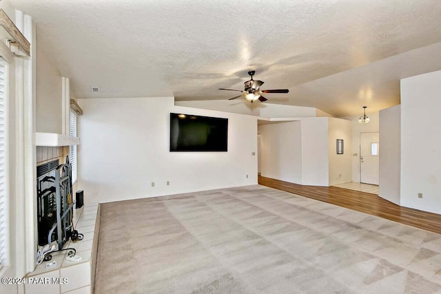 unfurnished living room with ceiling fan, a brick fireplace, a textured ceiling, vaulted ceiling, and light wood-type flooring