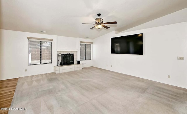 unfurnished living room with ceiling fan, a tiled fireplace, light carpet, and vaulted ceiling