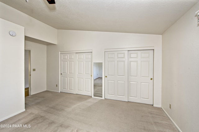 unfurnished bedroom featuring ceiling fan, lofted ceiling, light carpet, and two closets