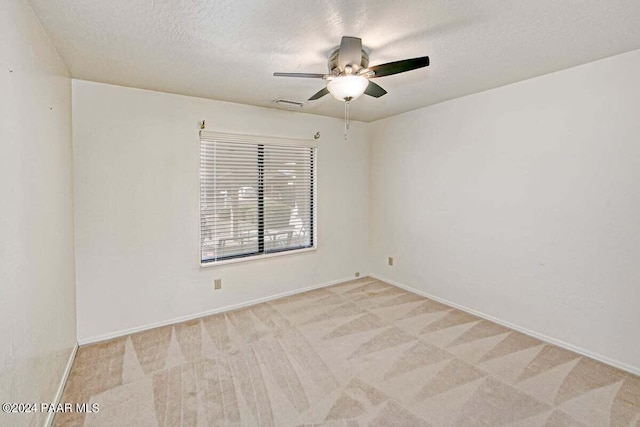 empty room with ceiling fan, light colored carpet, and a textured ceiling