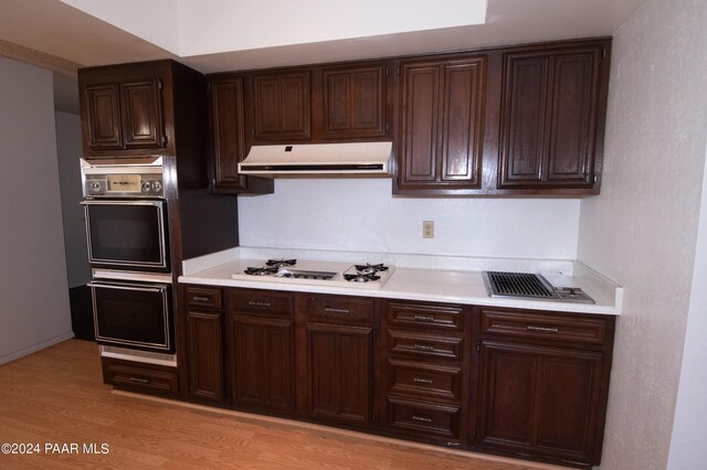 kitchen with white gas cooktop, black double oven, dark brown cabinets, and light wood-type flooring