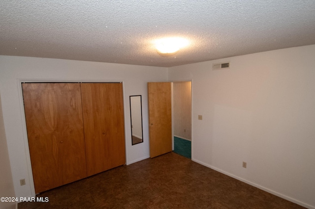 unfurnished bedroom with dark colored carpet, a textured ceiling, and a closet