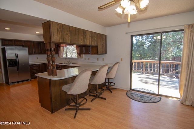 kitchen with a breakfast bar area, kitchen peninsula, stainless steel fridge, and light wood-type flooring