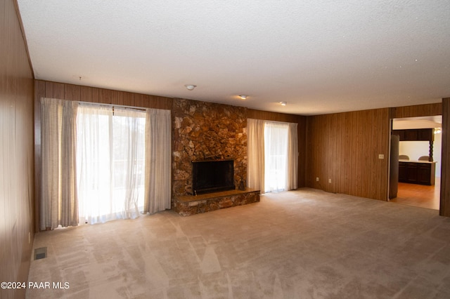 unfurnished living room featuring a stone fireplace, a wealth of natural light, light colored carpet, and a textured ceiling