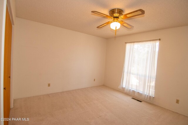 spare room with a textured ceiling, light colored carpet, and ceiling fan