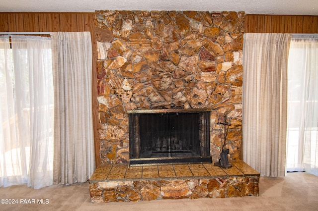 interior details featuring a fireplace, a textured ceiling, carpet flooring, and wood walls