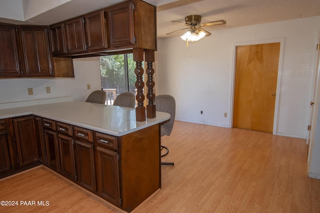 kitchen featuring ceiling fan, kitchen peninsula, a textured ceiling, a breakfast bar, and light wood-type flooring