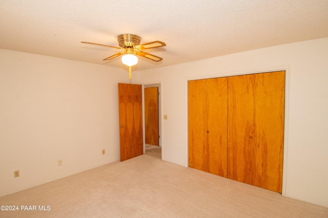 unfurnished bedroom featuring ceiling fan, light colored carpet, a textured ceiling, and a closet