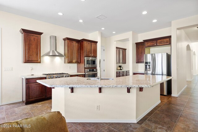 7590 E Traders Trl, Prescott Valley, AZ 86314 - kitchen featuring a breakfast bar area, a kitchen island with sink, wall chimney exhaust hood, and appliances with stainless steel finishes