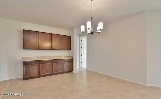 kitchen featuring light stone countertops, dark brown cabinets, an inviting chandelier, and hanging light fixtures