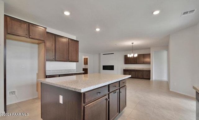 kitchen featuring hanging light fixtures, light stone counters, a chandelier, dark brown cabinets, and a kitchen island