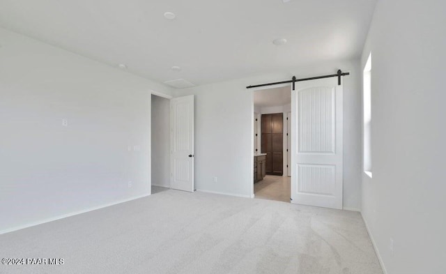 spare room featuring a barn door and light colored carpet