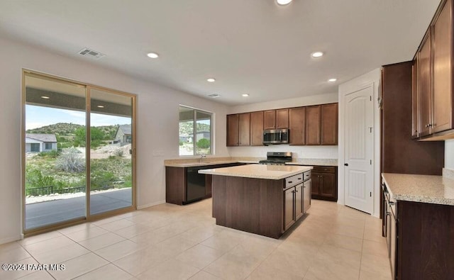 kitchen featuring stove, light stone counters, dark brown cabinetry, dishwasher, and a center island