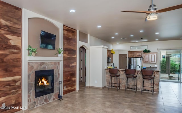 kitchen with ceiling fan, a stone fireplace, kitchen peninsula, a breakfast bar, and appliances with stainless steel finishes