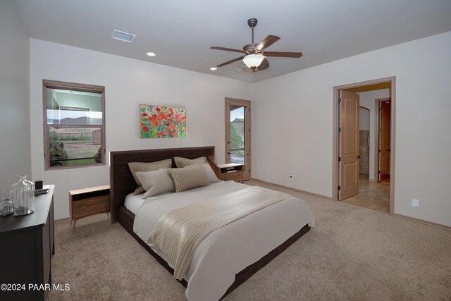 bedroom featuring light colored carpet, ensuite bath, and ceiling fan