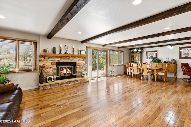 living area with recessed lighting, hardwood / wood-style floors, a stone fireplace, beamed ceiling, and baseboards
