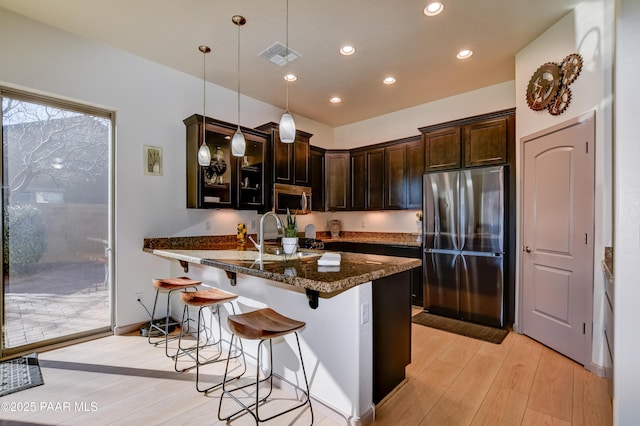 kitchen featuring pendant lighting, stainless steel appliances, dark stone countertops, a kitchen breakfast bar, and sink