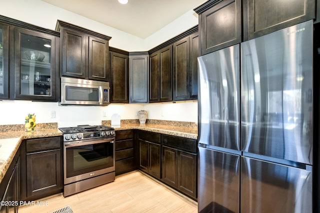 kitchen featuring light stone counters, dark brown cabinets, stainless steel appliances, and light hardwood / wood-style floors