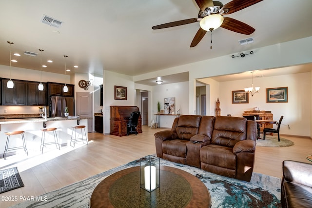 living room with sink, ceiling fan with notable chandelier, and light hardwood / wood-style flooring