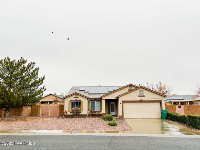 ranch-style home with stucco siding, concrete driveway, an attached garage, roof mounted solar panels, and fence private yard