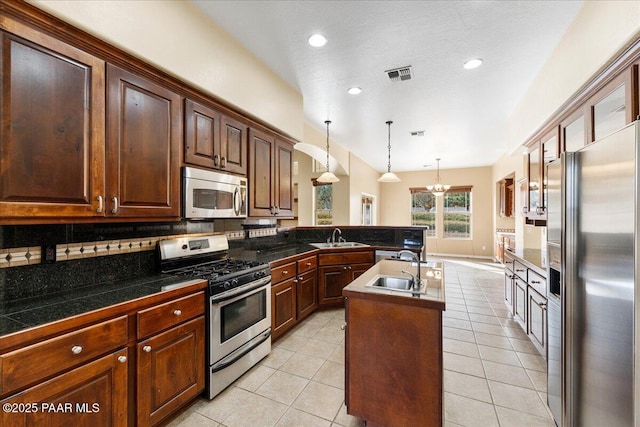 kitchen featuring appliances with stainless steel finishes, pendant lighting, tasteful backsplash, sink, and a kitchen island with sink