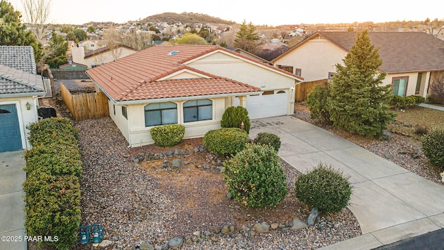 view of front facade with fence, a tile roof, stucco siding, a garage, and driveway