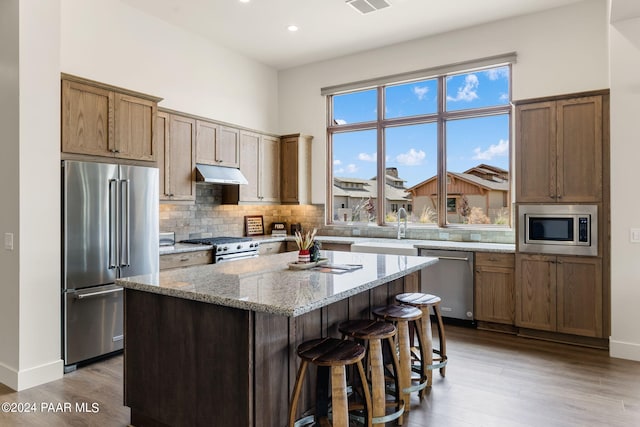 kitchen with decorative backsplash, light stone countertops, light wood-type flooring, premium appliances, and a center island