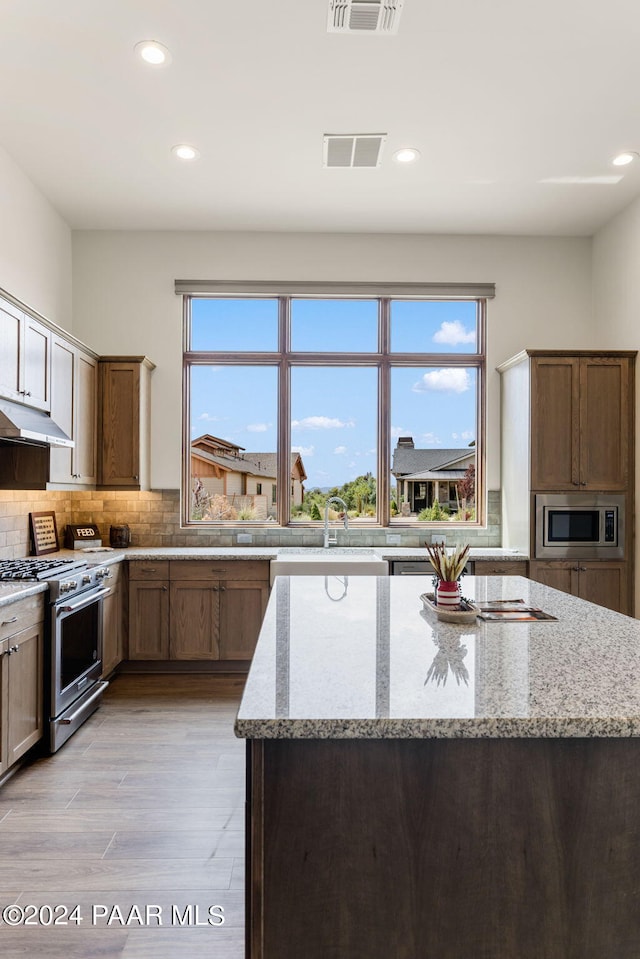 kitchen with backsplash, sink, light hardwood / wood-style floors, light stone counters, and stainless steel appliances