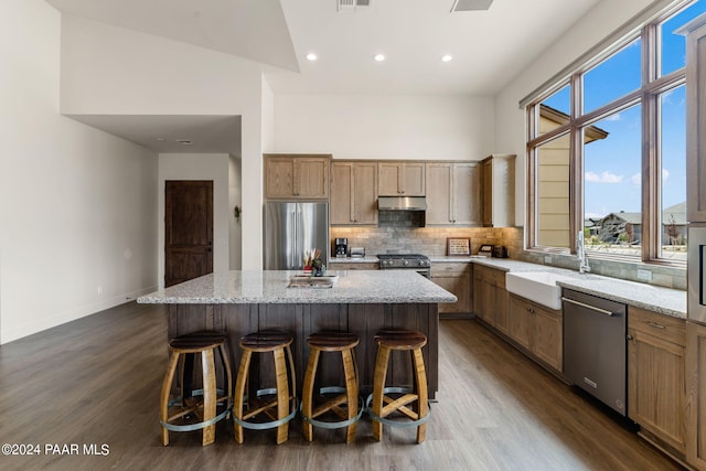 kitchen with a kitchen island, dark hardwood / wood-style flooring, light stone countertops, and stainless steel appliances