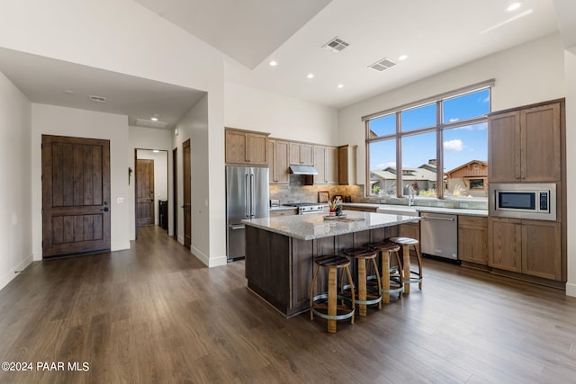 kitchen with dark hardwood / wood-style flooring, light stone counters, a breakfast bar, stainless steel appliances, and a kitchen island